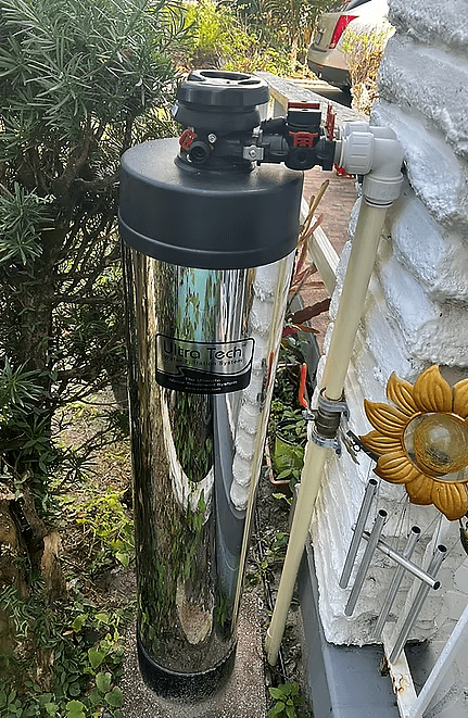 Stainless steel water filter housing installed outdoors among plants
