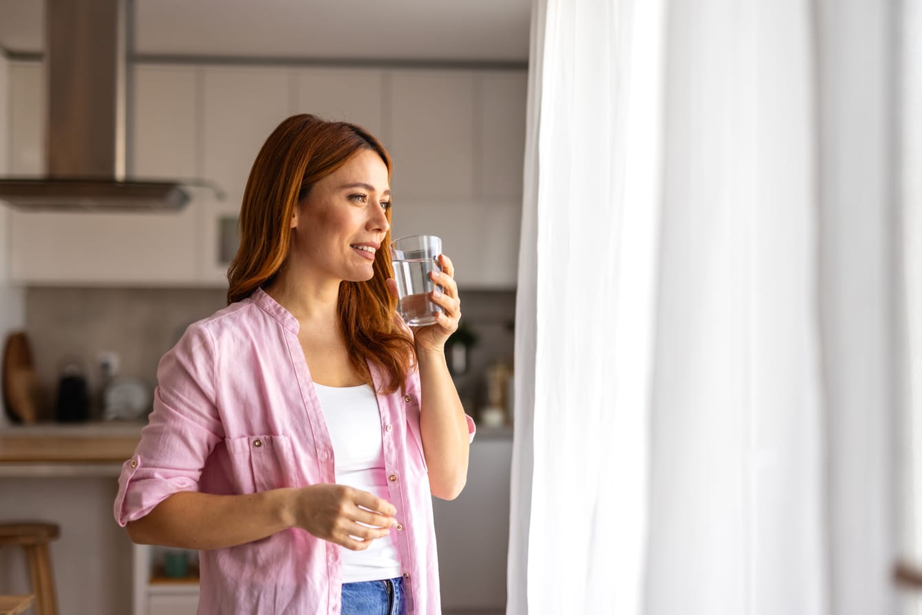 Woman drinking a glass of filtered water at home